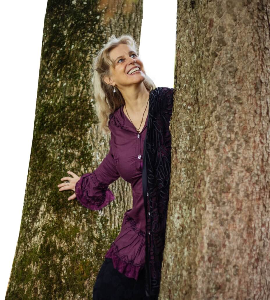 Anja Cantánima lachend in der Natur zwischen zwei Bäumen 
